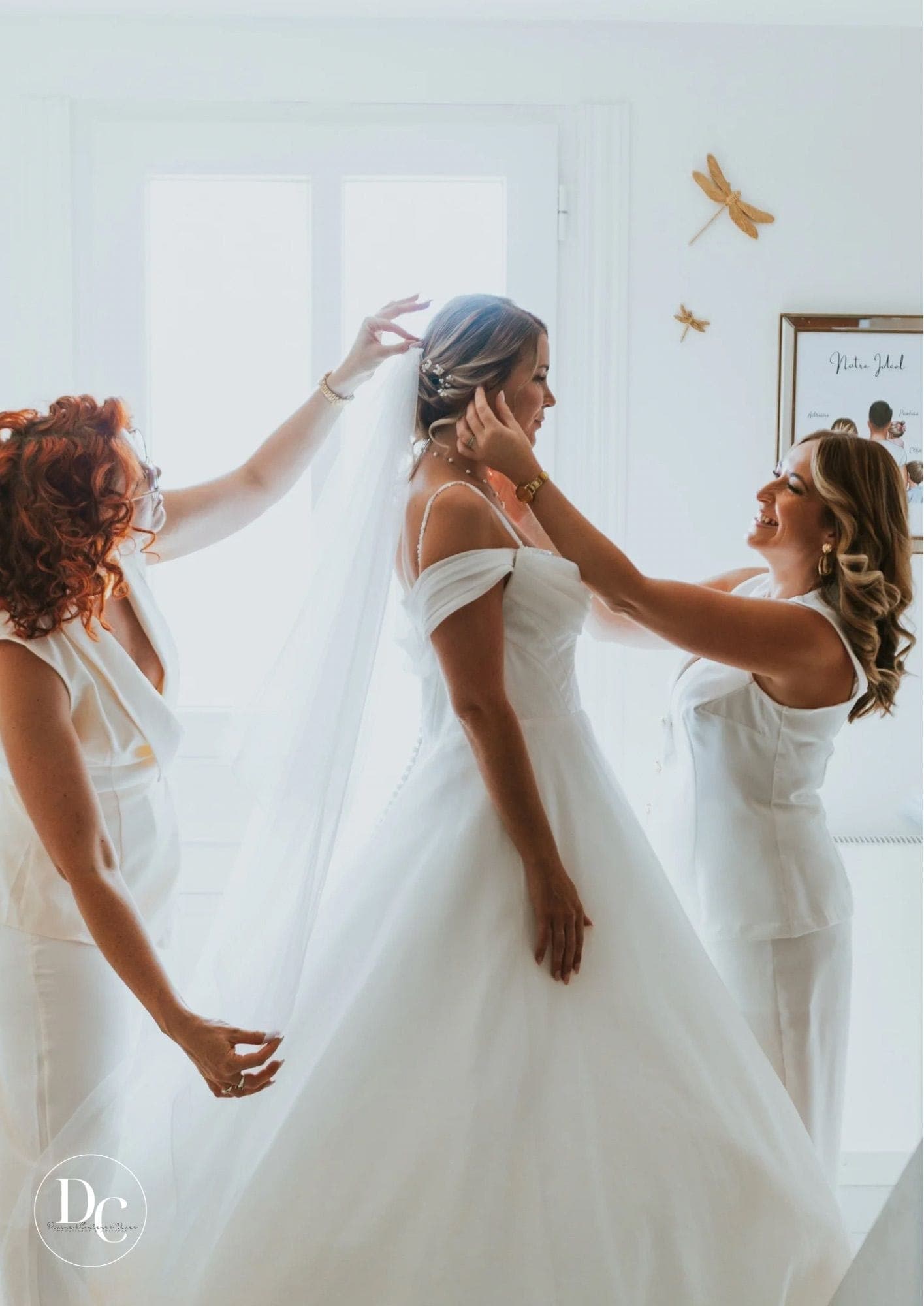 Camille et une témoin ajustent le voile de la mariée avant la cérémonie, chignon bas orné de perles