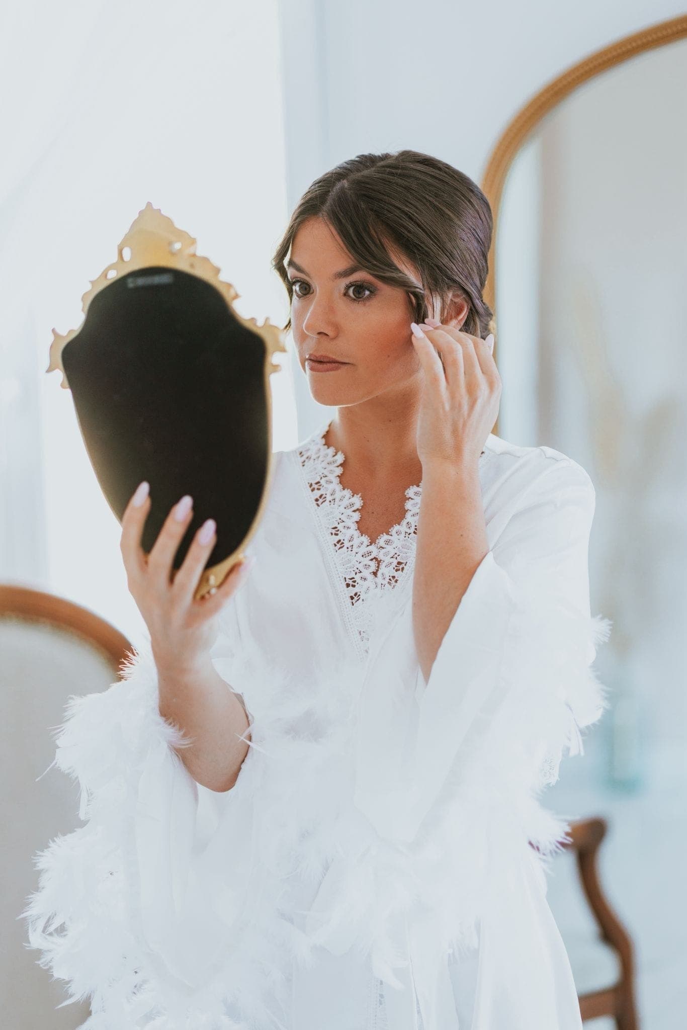 La mariée vérifie sa coiffure dans un miroir ancien, chignon souple et mèches ondulées